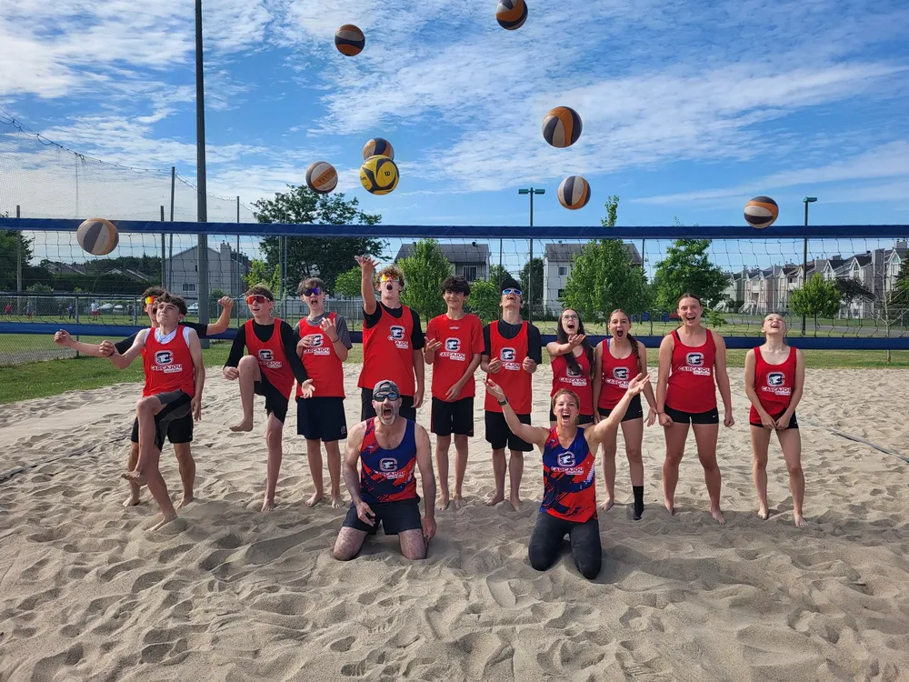 Groupe de jeunes sur un terrain de sable, ballons lancés en l’air